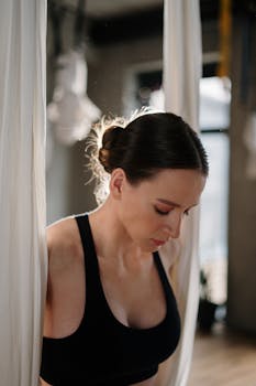 Focused woman in black outfit practicing aerial yoga in a sunlit studio.