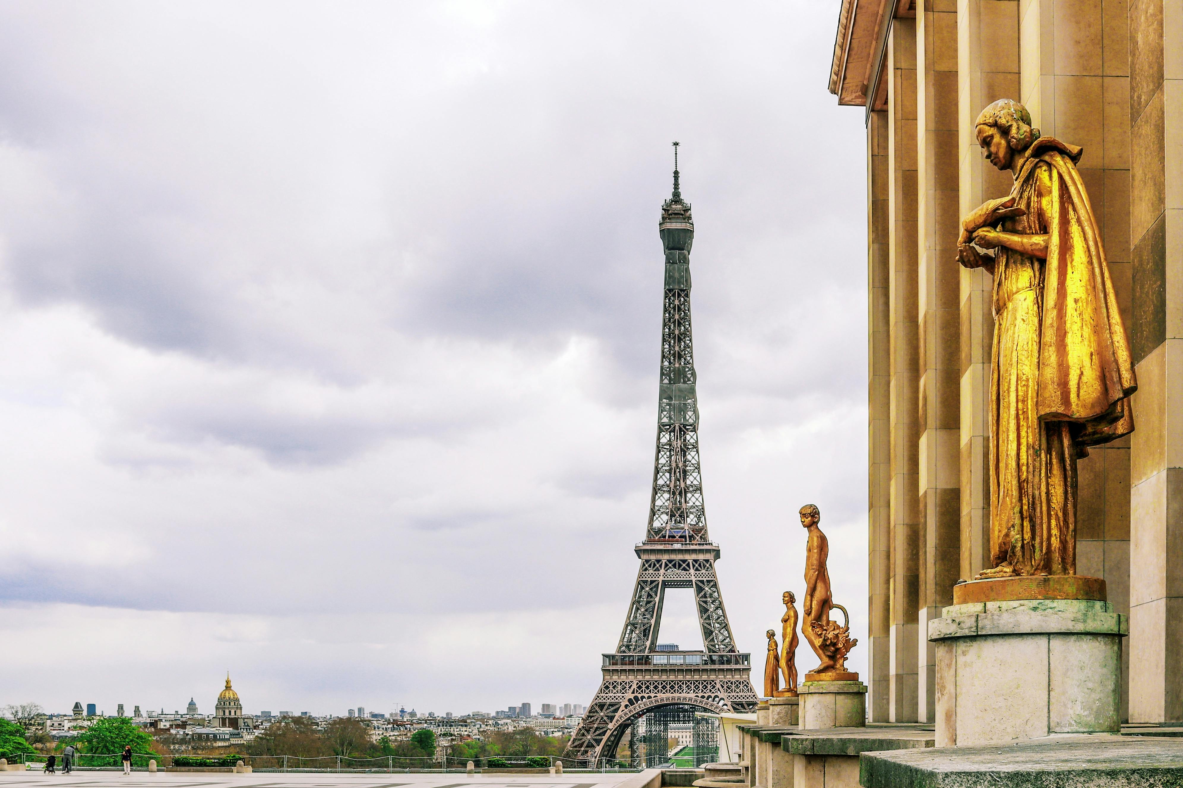Famous Eiffel Tower and ancient golden statues under overcast sky