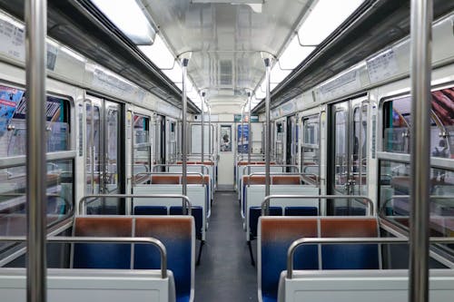 Empty illuminated subway train with seats and metal railings stopped on platform at station