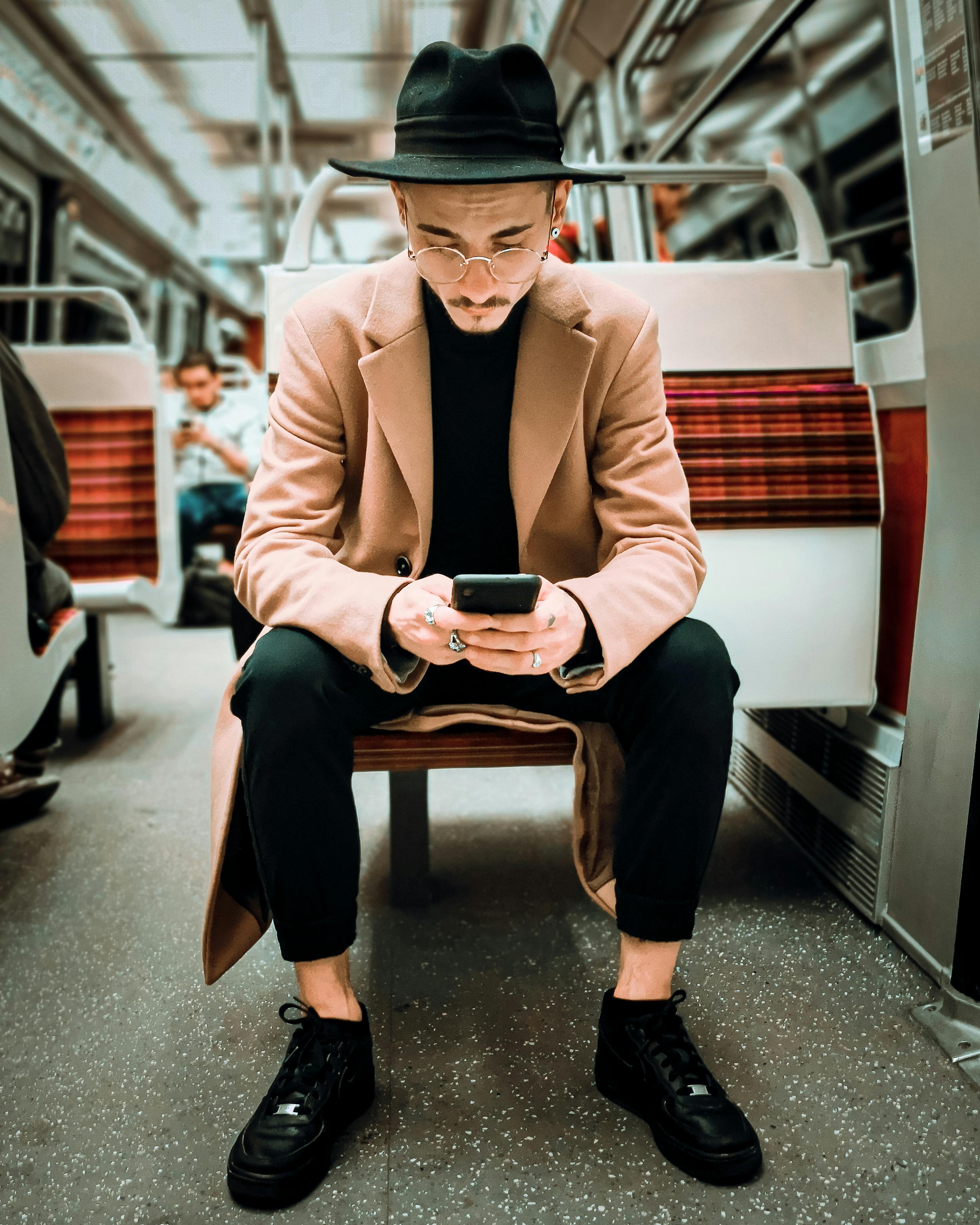 elegant man in hat and eyeglasses using smartphone in modern train