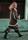 Side view of stylish young female in trendy sheepskin coat walking on paved street and looking at camera