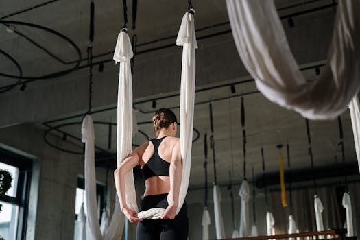 Woman practicing aerial yoga in a contemporary gym, focusing on flexibility and wellness.