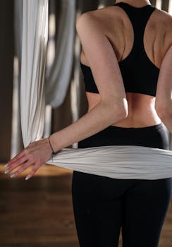 A woman engaged in aerial yoga practice, focusing on flexibility and core strength.