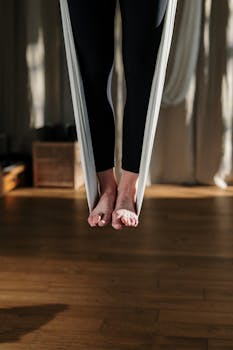 Feet suspended in a yoga hammock indoors, promoting balance and wellness.
