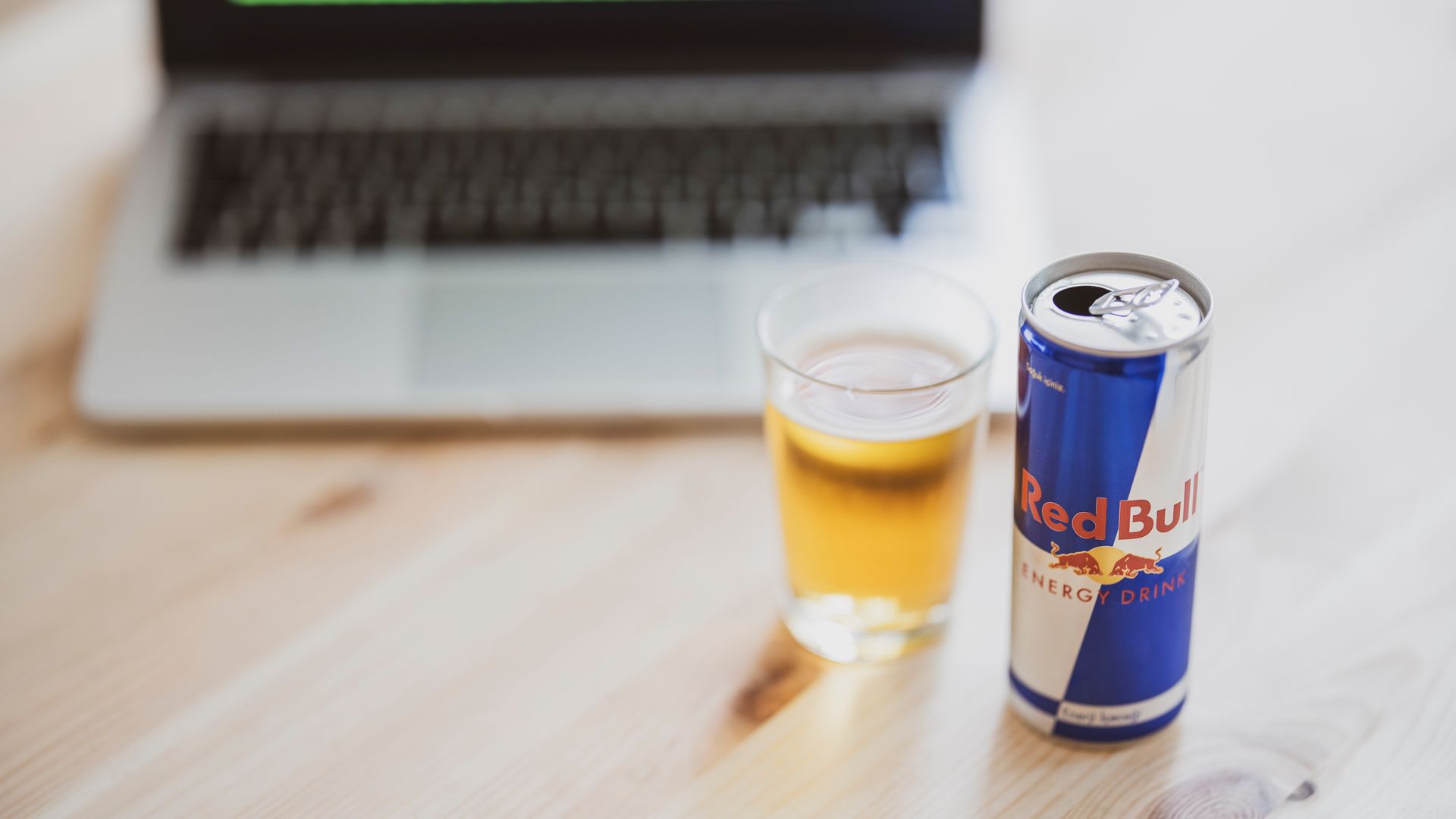 Modafinil vs Energy Drinks: Which Boosts Energy Better? A can of Red Bull and a glass on a wooden desk with a blurred laptop in the background — modafinil vs energy drinks