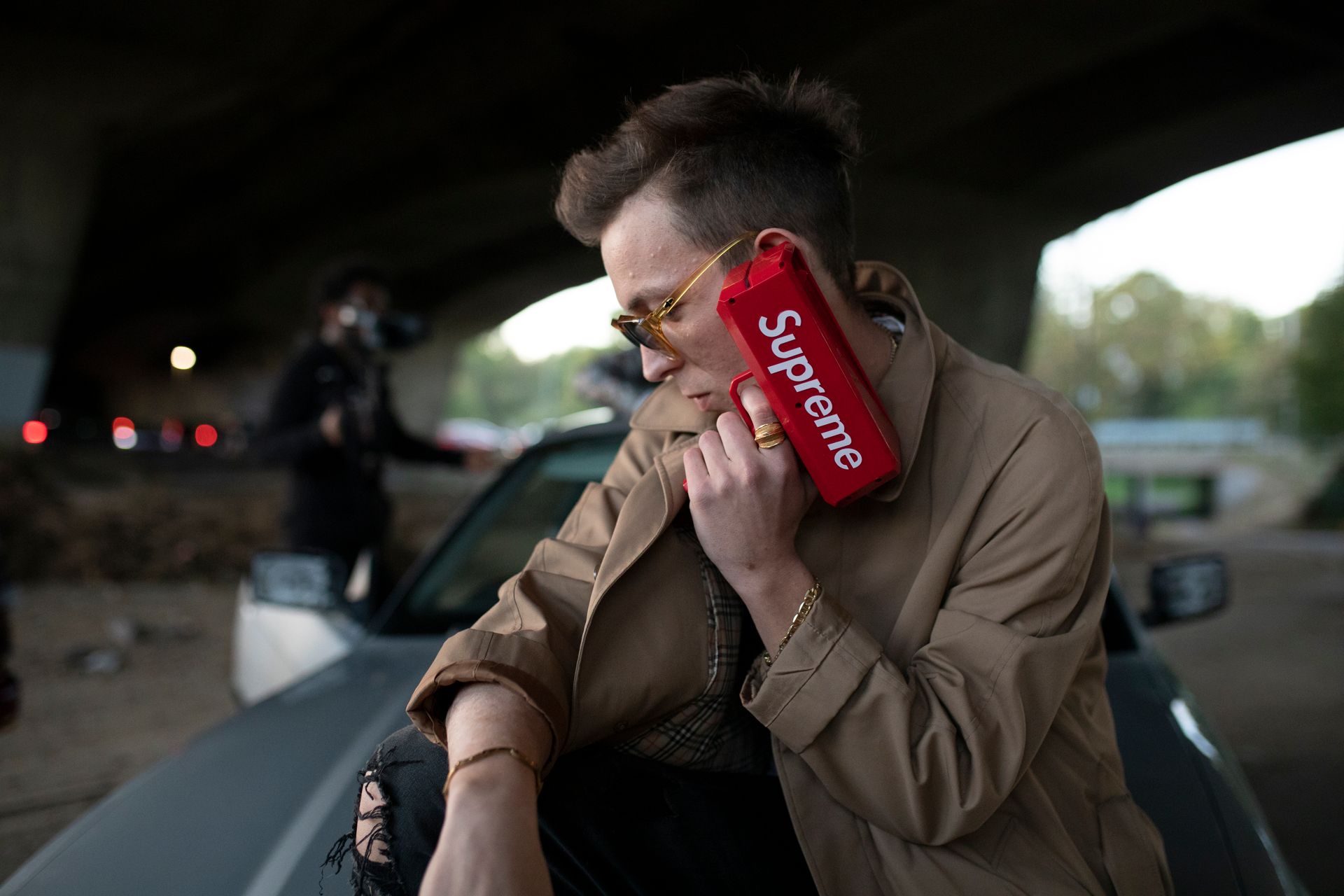 Stylish young man posing outdoors with a red Supreme toy gun, exuding urban fashion vibes.