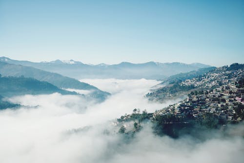 Peaceful landscape of remote town on slope of green mountain in highland valley covered with fog