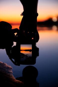 A silhouette of a camera capturing a sunset lake reflection in Türkiye. Vibrant colors and serene scene.