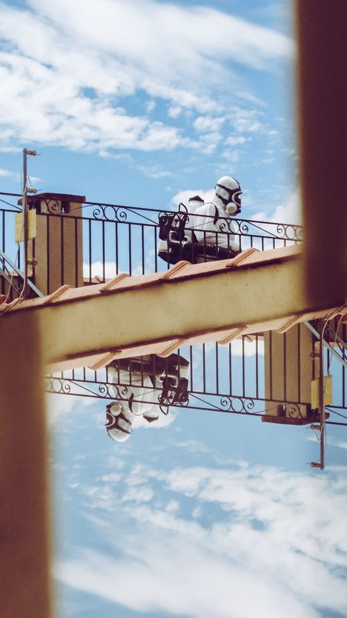Free Person in pandemic protective gear reflected on balcony railing against blue sky with clouds. Stock Photo