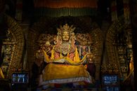 Golden statue of Buddha in colorful clothes placed against ornamental arches in ancient monastery