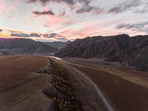 Drone view of narrow road between desert mountain slopes and valleys during amazing sundown