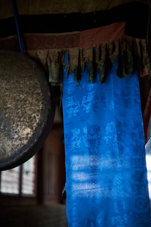 Interior of ancient Buddhist temple with hanging traditional sacred silk scarf and metal gong