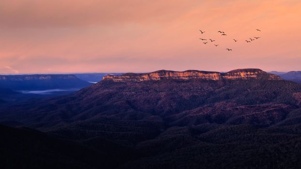 A stunning mountainous landscape with birds flying at sunset, capturing nature's serene beauty.