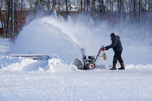 Free Full body man in warm clothes walking with snow thrower while cleaning yard in town Stock Photo