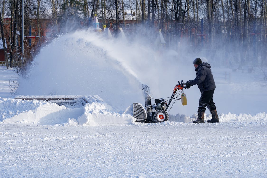 Free Full body man in warm clothes walking with snow thrower while cleaning yard in town Stock Photo