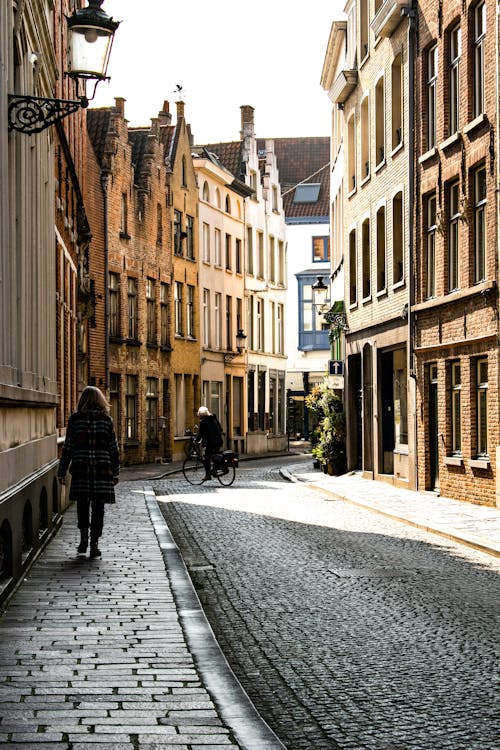 Free Calm paved narrow street of old town with people walking in morning sunlight Stock Photo