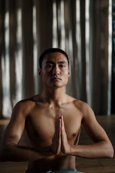 Shirtless Asian man practicing yoga in a serene indoor setting, promoting wellness.