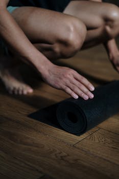 Close-up of a man rolling up a yoga mat on a wooden floor in a yoga studio.