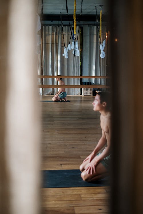 Topless Man Sitting on Brown Wooden Floor