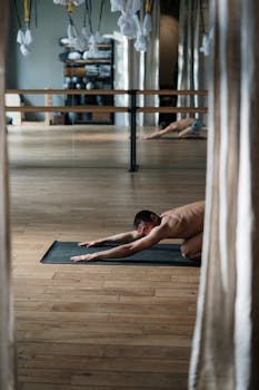 Shirtless man practicing yoga on mat in a studio, reflecting health and wellness.