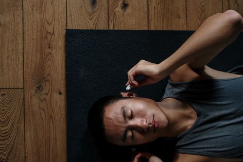 Free An Asian man relaxing with headphones, lying on a yoga mat in a serene indoor setting. Stock Photo
