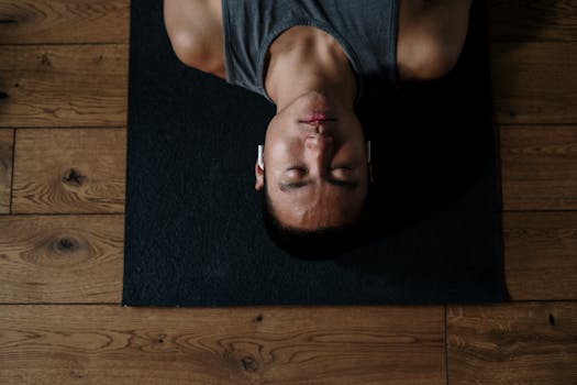 Young man meditating indoors on a yoga mat with headphones, promoting wellness and relaxation.