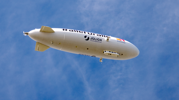 From below contemporary blimp with advertisements flying in cloudy blue sky on sunny day