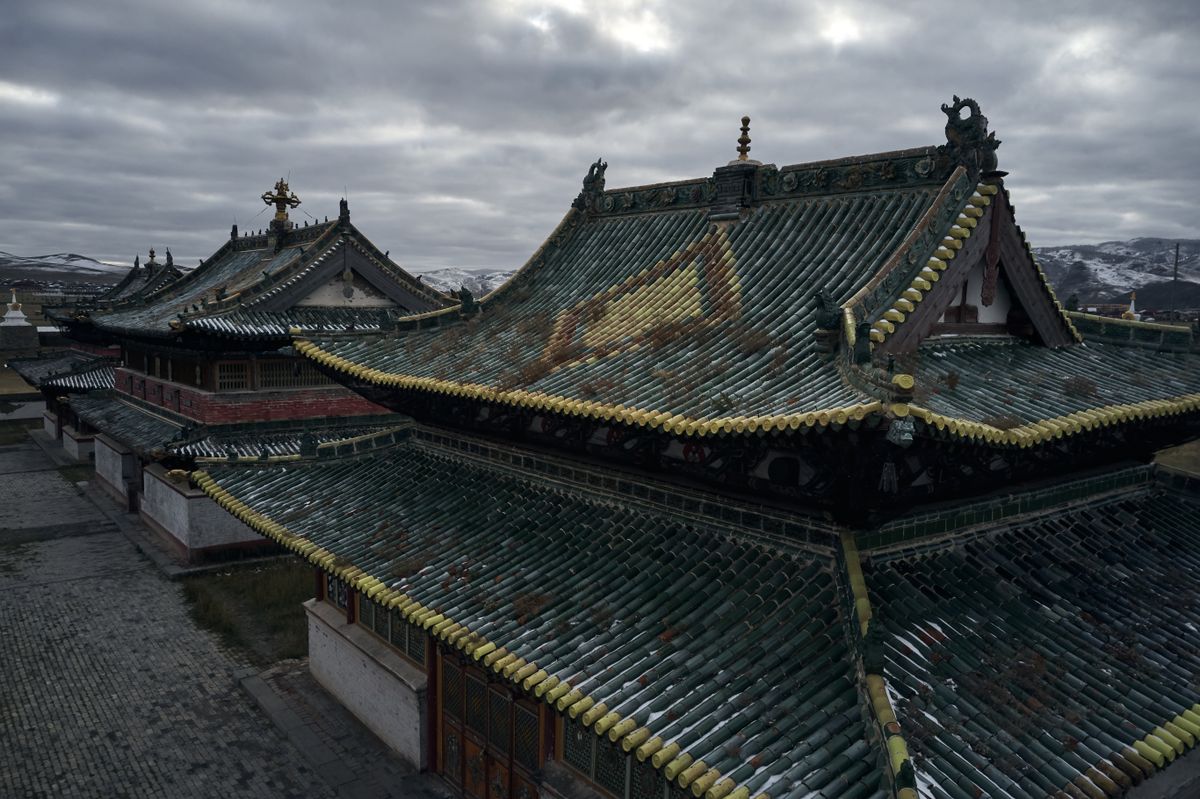 The green-and-gold tiled rooftops of Erdene Zuu Monastery under a flat grey sky, temple buildings raised from the same quarried stone that once built Karakorum.