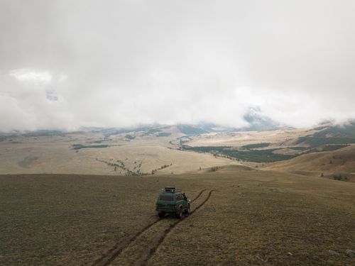 Free Aerial view of old green SUV car driving along empty endless valley under thick clouds Stock Photo