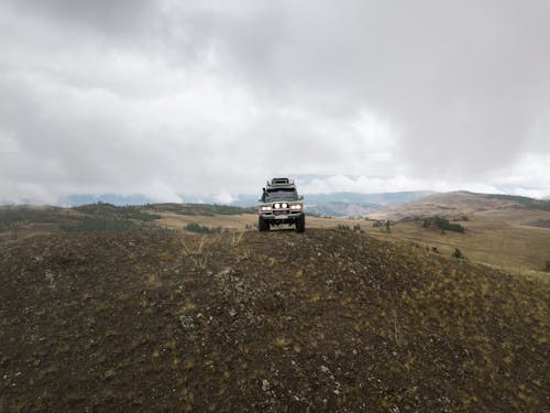 Old SUV car parked on top of hill in mountainous terrain on cloudy day