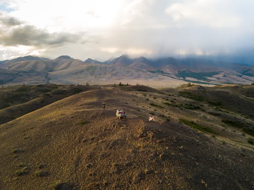 Aerial view of car and anonymous travelers walking on top of hill against mountain ridges and desert valleys