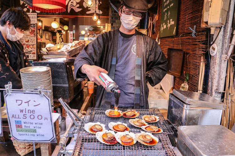 Asian Man In Mask Frying Clams On Street Market