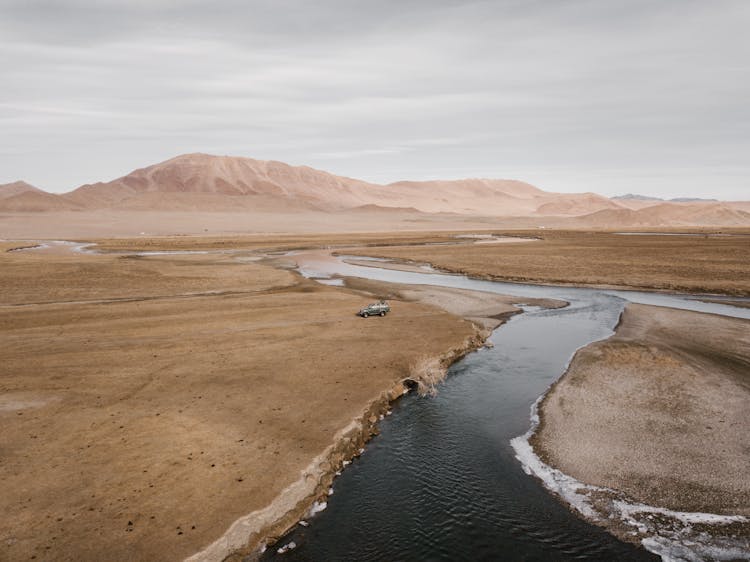 Winding River In Vast Lands With Lonely Car On Bank