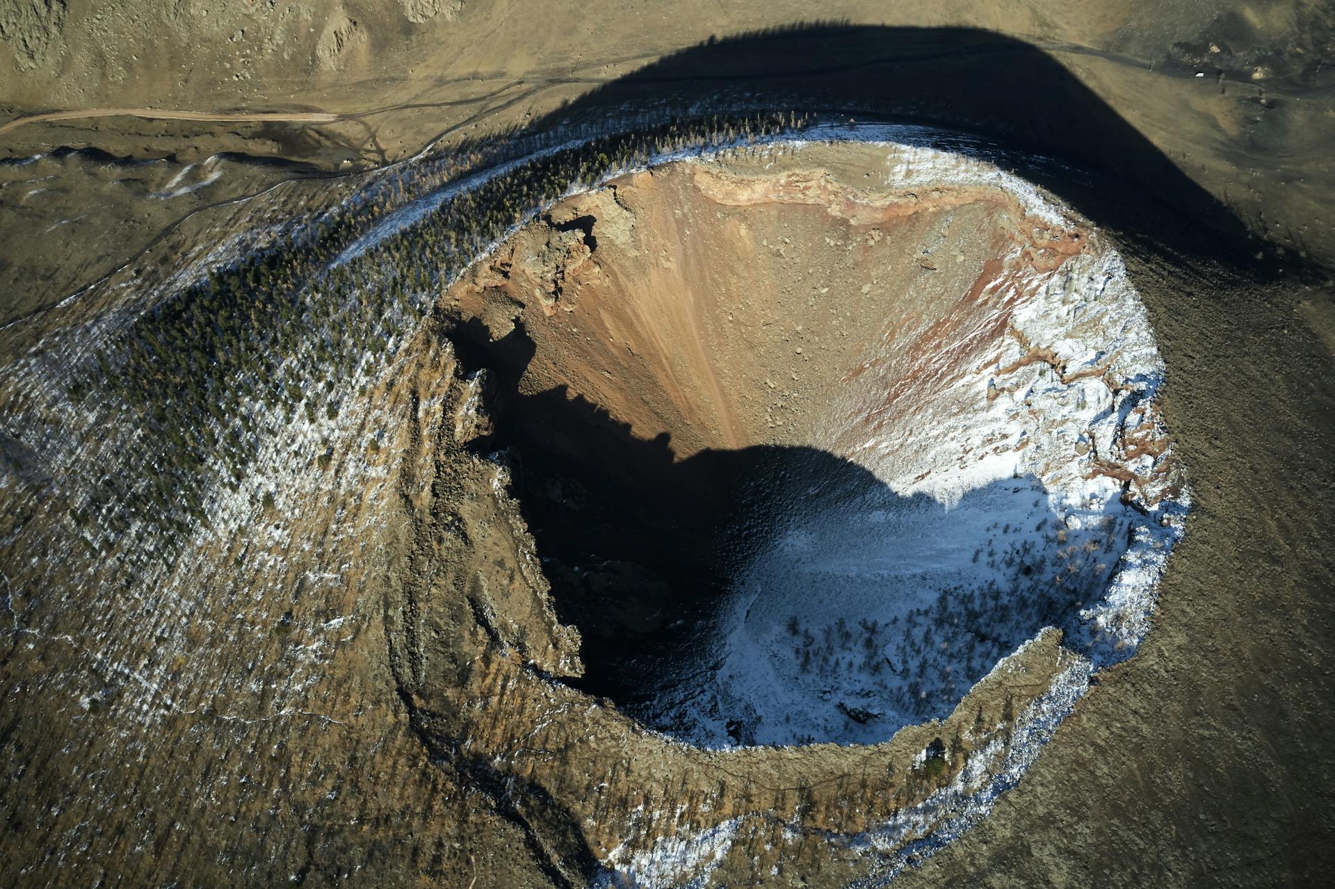 Breathtaking aerial view of Khorgo Uul Mongolian extinct volcano forested on sides and covered with snow in bright sunlight