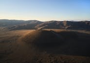 Dormant volcano in quiet desolate valley surrounded with mountain ranges in sunlight under clear blue sky