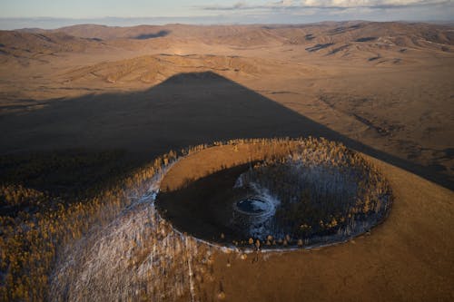 Aerial view of Khorgo extinct volcano grown with forest and covered with snow casting huge dark shadow on valley in national park in Mongolia