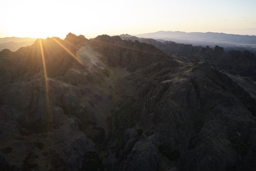 Majestic drone view of mountain range almost plunged into darkness touched by last sunbeam of setting sun causing lens flare