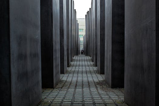 A lone figure walks through the somber Holocaust Memorial in Berlin, surrounded by towering concrete slabs.