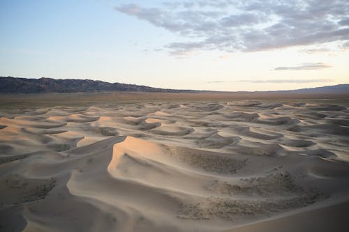Scenic view of sand dunes with loose texture in desert near mountain under cloudy sky in evening time