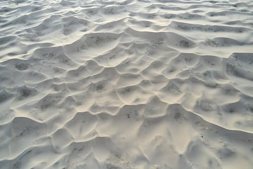 From above of textured light grey dunes of sand in remote calm desert in afternoon