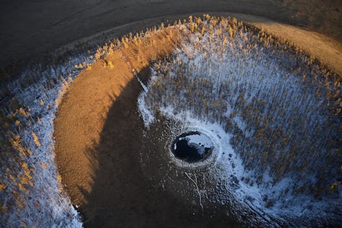 From above of round black puddle with glares on surface located in sand cavity in evening time