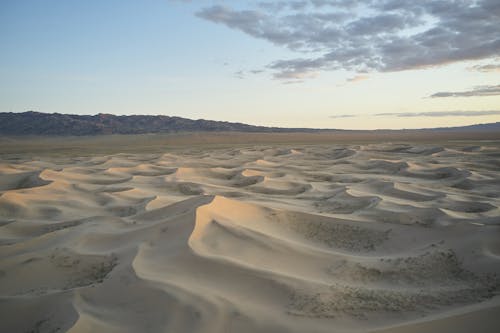 Picturesque view of dry sand hills with loose texture located near ridge under blue sky with clouds in evening time