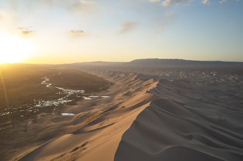 Breathtaking view of sand dunes with dry texture and wavy surface located in desert with arid soil at sundown under cloudy sky