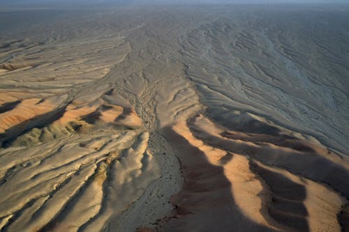 From above of dry terrain with arid soil covered with sand forming wavy lines on surface in daylight