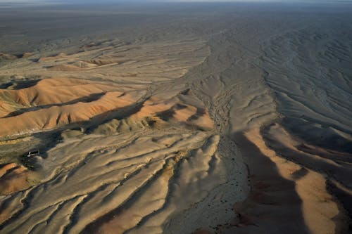 Top view of desolated sand ribbed surface with barren soil and small puddles in desert in daylight