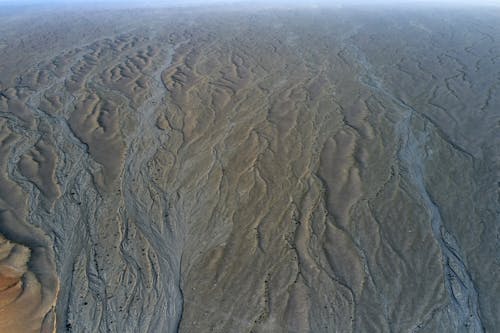 Drone view of desert with dry sand and loose texture forming curve lines on horizon under serene sky