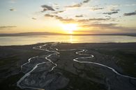 Picturesque view of lake with river tributaries passing by sand surface and ridge behind under cloudy sky at bright sundown