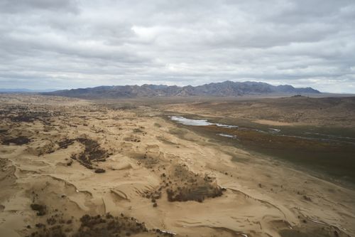 Free Aerial view of rough sandy semidesert with dry vegetation and curvy river against mountains under cloudy sky Stock Photo