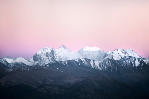 Majestic view of snowy mountains peaks near green highlands in dusk under scenic bright purple cloudy sky