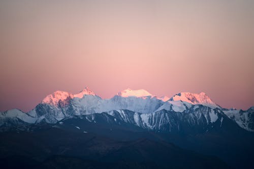 Wonderful view mountains ridge covered with white snow enlightened with bright pink sunrise sun under purple sky